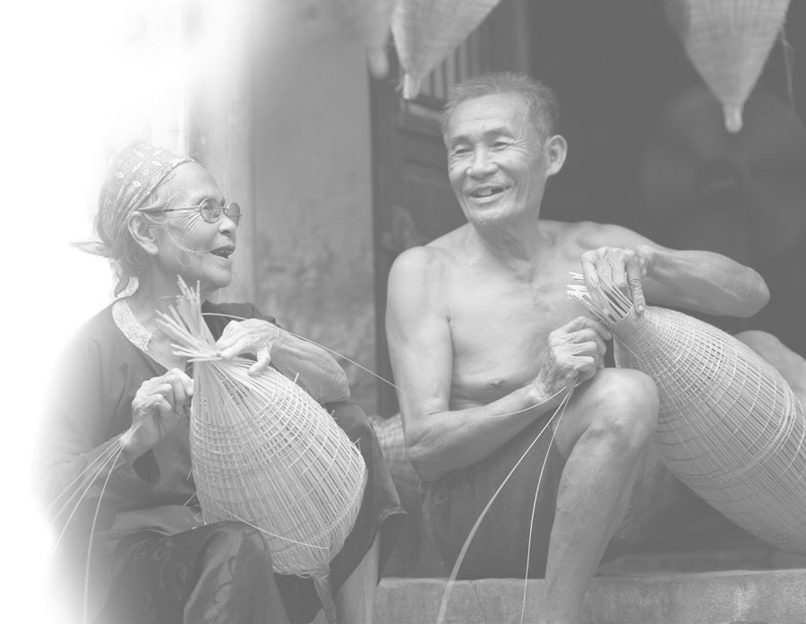 Two artisans sitting together, hand-weaving bamboo fish traps outside a village workshop.