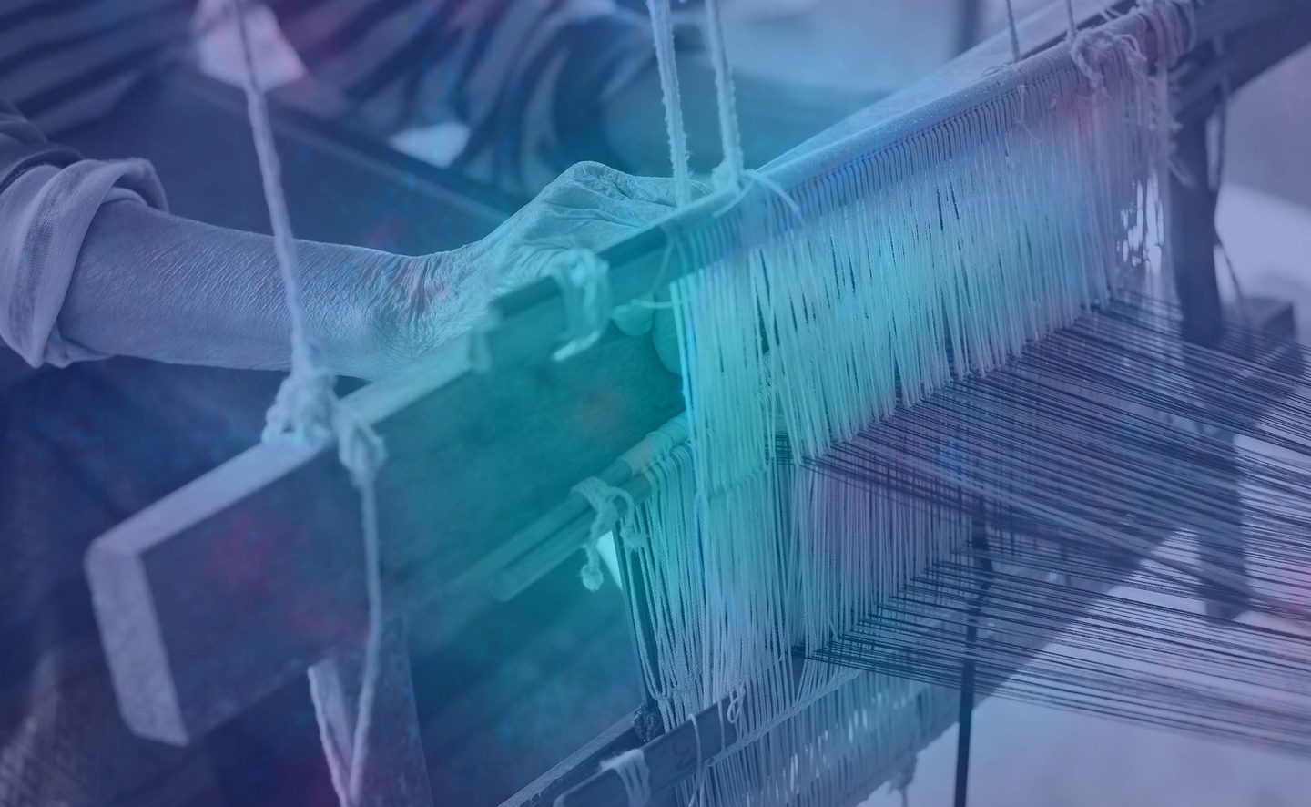An artisan's hands guiding thread across a traditional wooden handloom.
