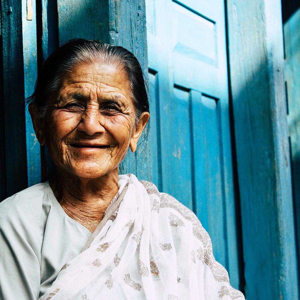 Portrait of an elderly woman in a white shawl smiling in a doorway.